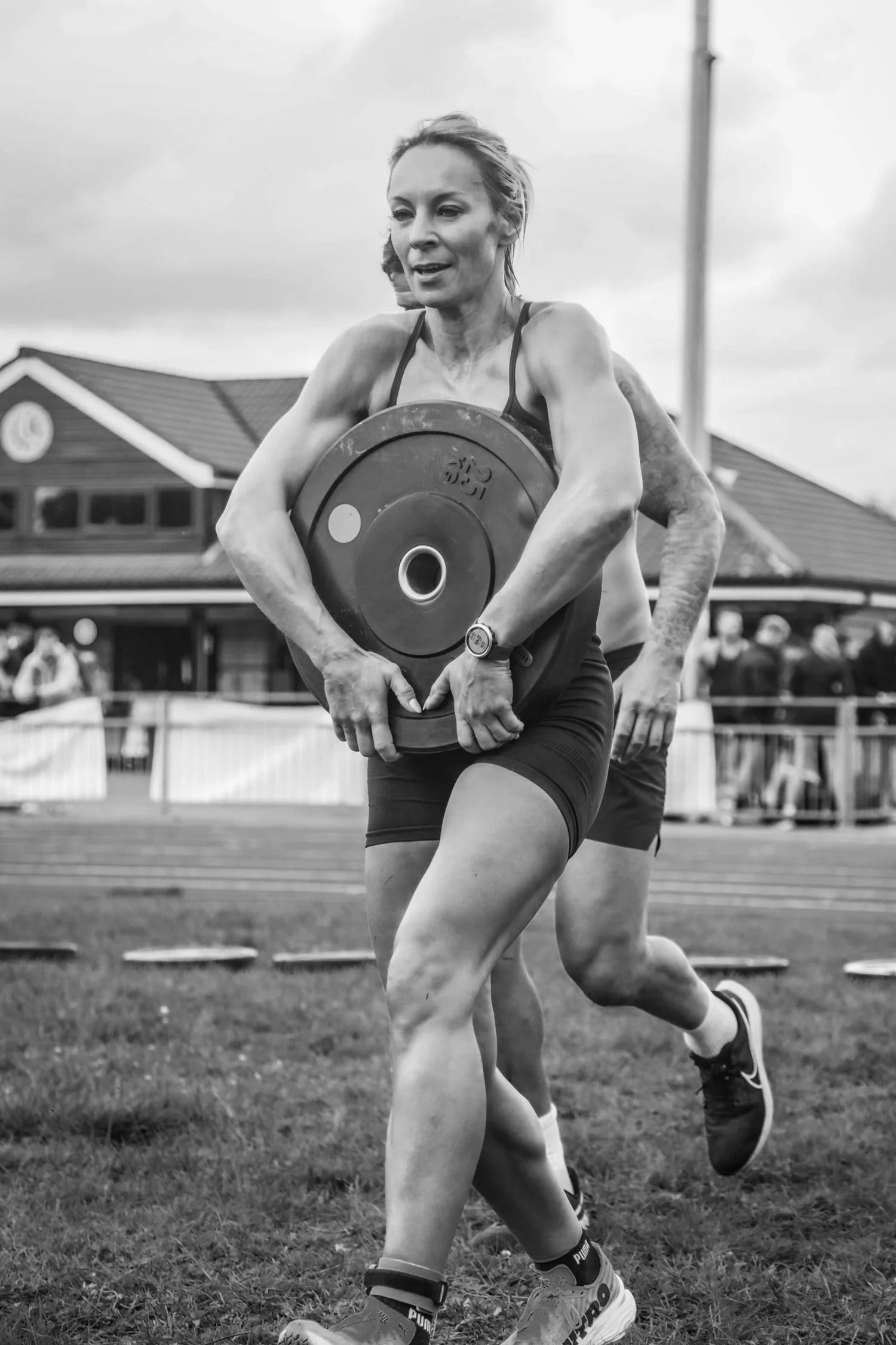 Atleta a transportar um disco de peso na parte da frente do corpo, no exercício «Front Carry Labour»